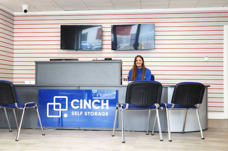 Storage space Sittingbourne. Image shows Cinch storage employee sitting at reception desk smiling. 