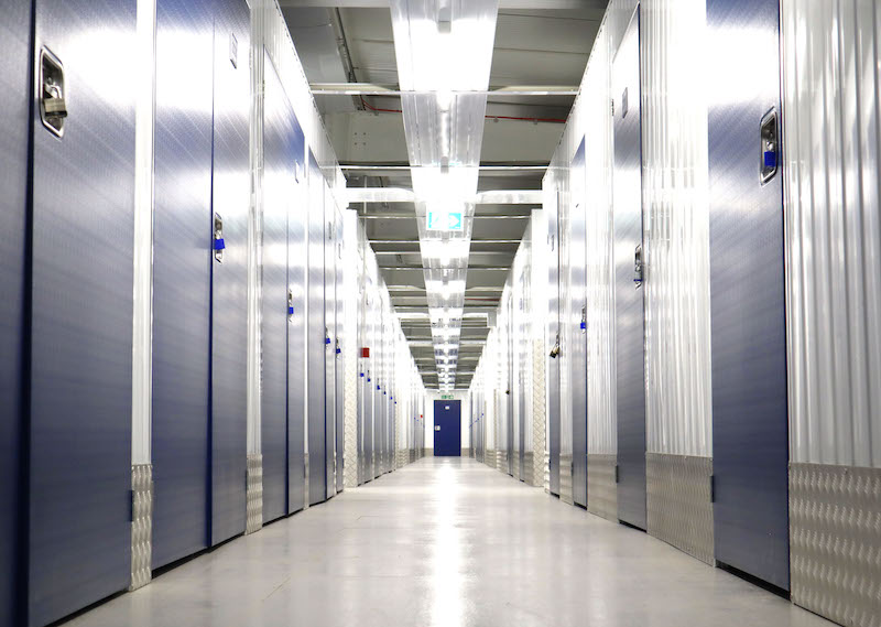 Storage units Bedford. Image shows a corridor of a storage facility with blue doored storage units on either side. 