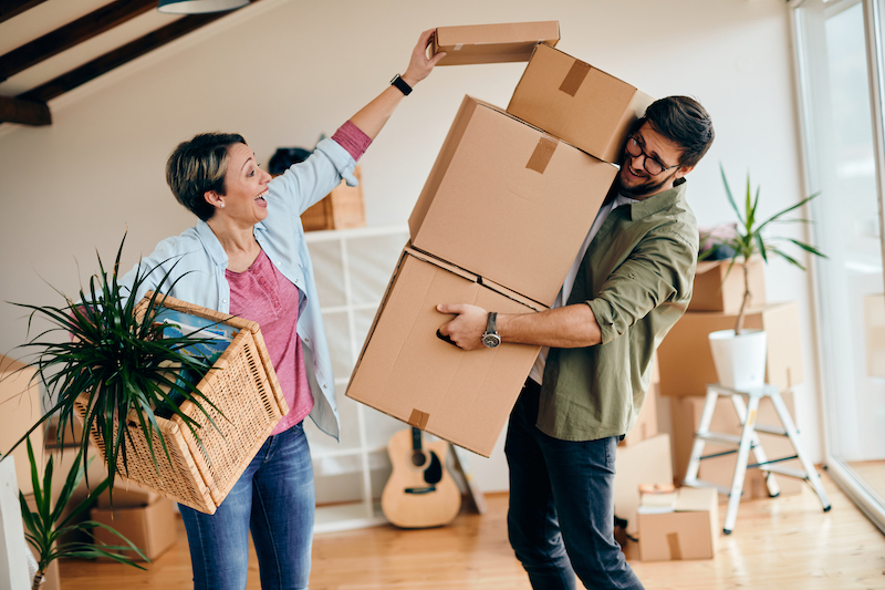 House move storage Bedford. Image shows a woman piling cardboard boxes on top of a pile of them that a man is carrying, moving house.