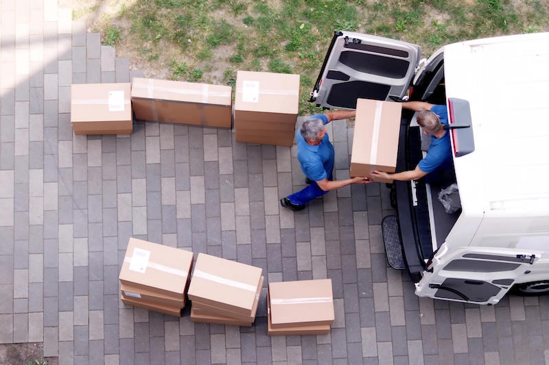 House move storage Houghton Regis. Image shows two men passing eachother a cardboard box from a white van, moving people into their home.