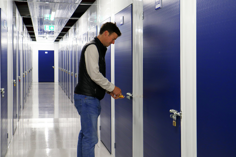 Storage unit to rent Dunstable. Image shows a man unlocking his storage unit with a blue door.