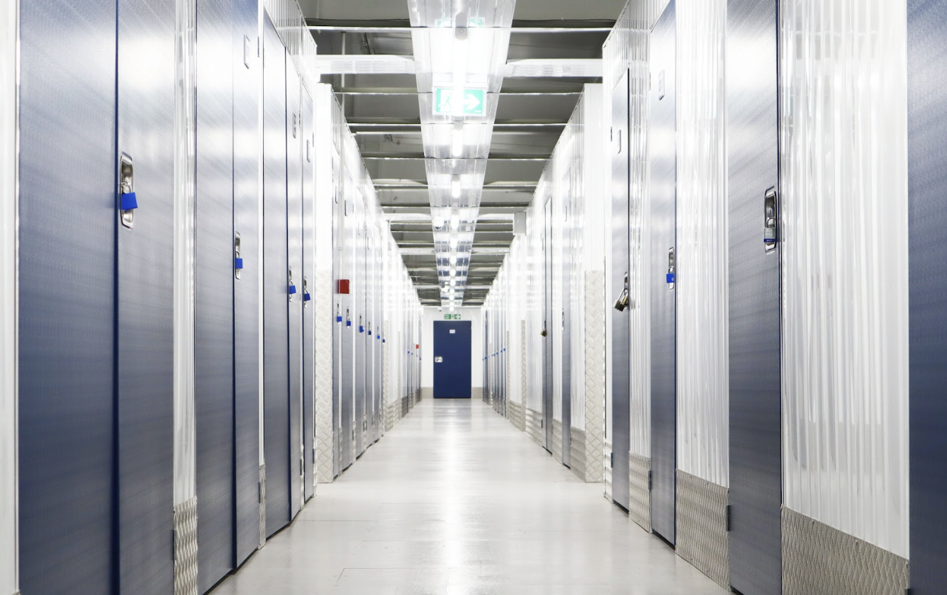 Storage units in Bedford. Image shows interior of storage facility with a corridor of storage units with blue doors on either side.