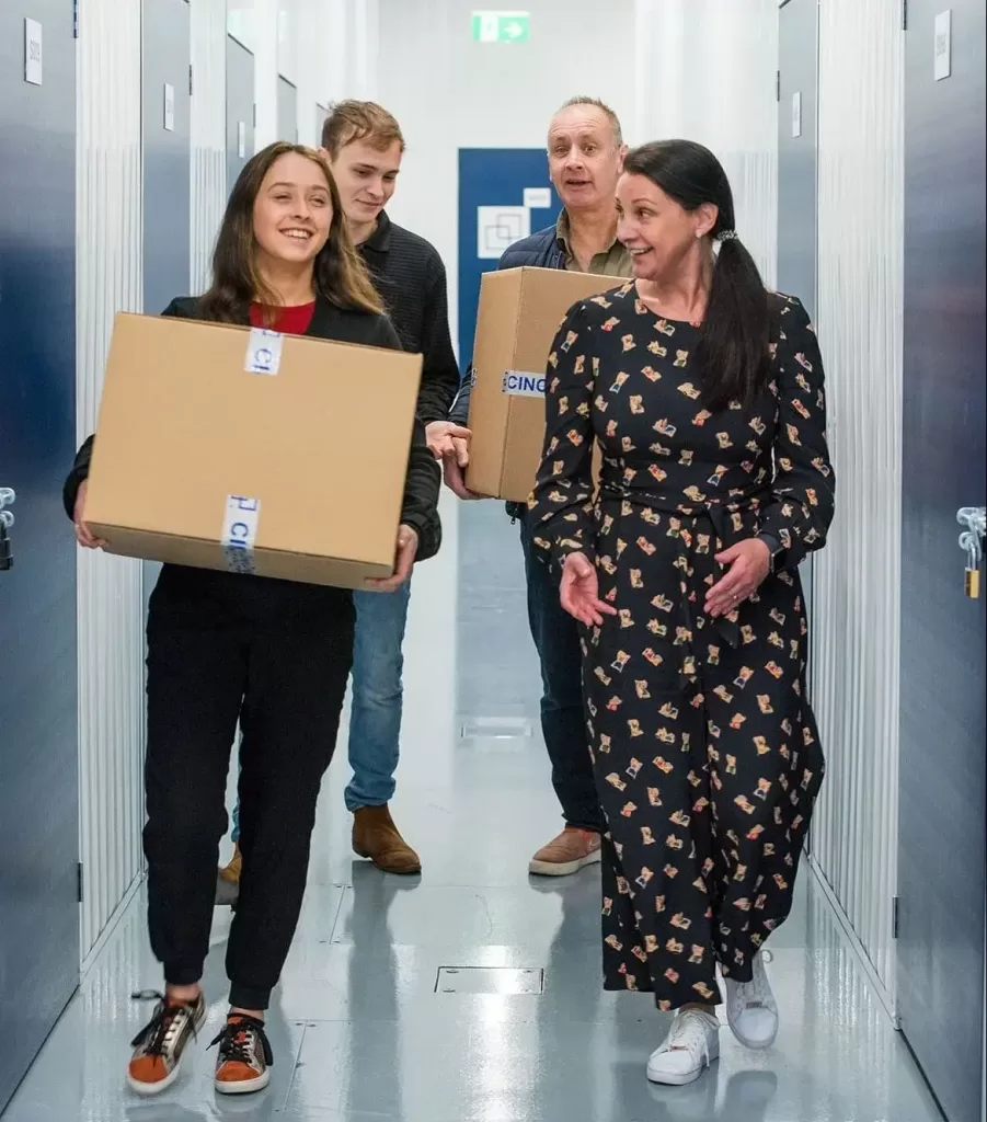 Two people carrying boxes while talking with their friends through a hallway