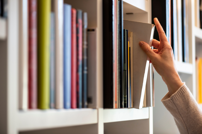 Low cost self storage in Bedford. Image shows the hand of woman searching for a book on a shelf