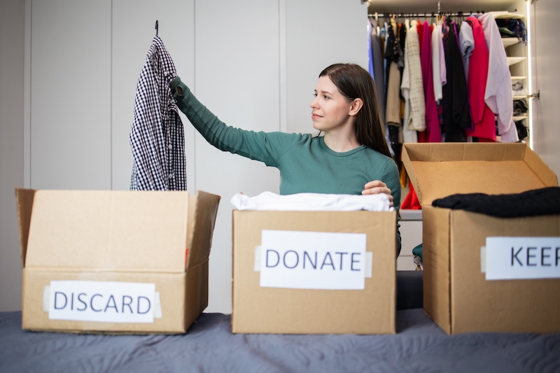 The ultimate decluttering checklist. Image shows a woman sorting clothes into different piles, discard, donate keep.