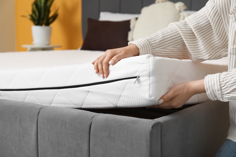 How to store a mattress. Image shows a woman holding the edge of a mattress up away from the bed base.