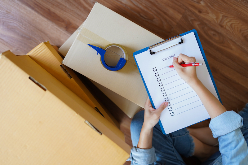 Moving house checklist. Image shows someone with a clipboard writing their moving house checklist surrounded by packing boxes.