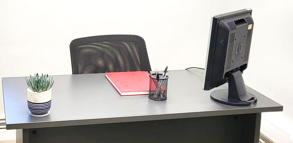 Office space to rent Enfield. Image shows a black desk and chair with a red notebook on the desk.