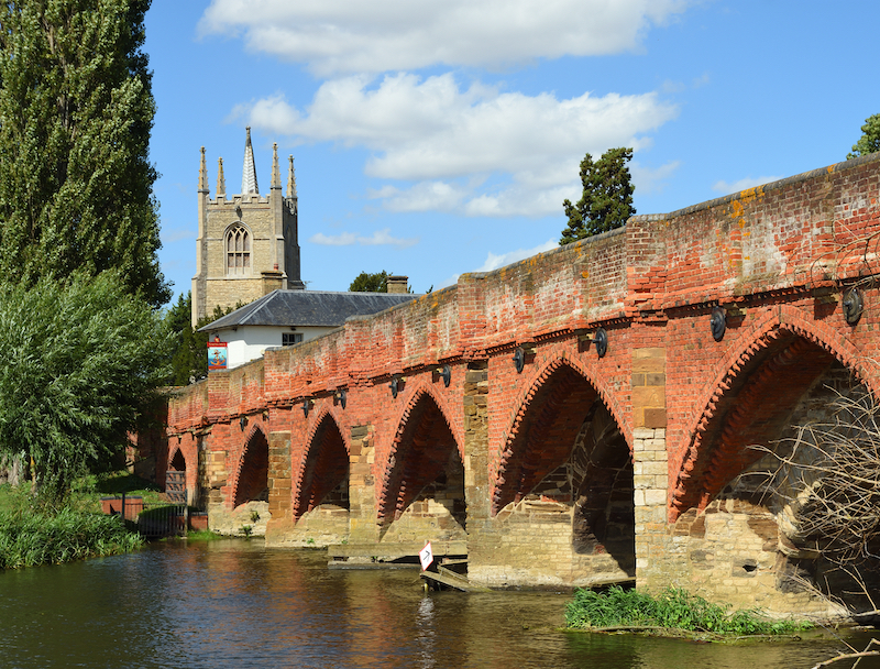 5 questions about living in Bedford. Image shows Great Barford Packhorse Bridge and All Saints Church Tower. Bedfordshire England.