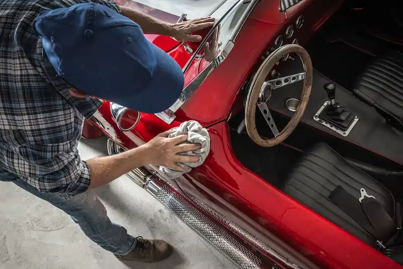 Classic car storage. Image shows a red classic car being cleaned by a man wearing a navy blue hat.