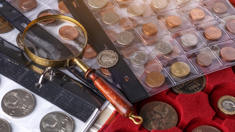 How to store collectables. Image shows a folder with collectable coins and a magnifying glass lying on top.