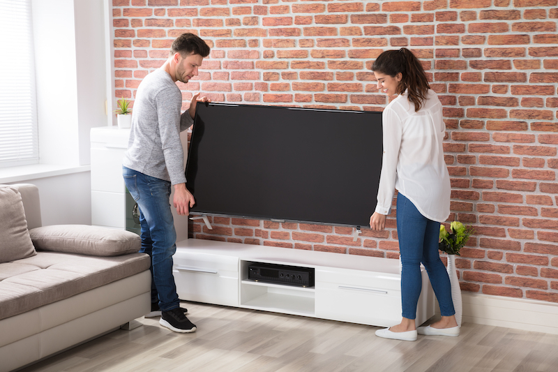 How to pack a tv for moving. Image shows a couple lifting up their tv ready to pack it up into storage.