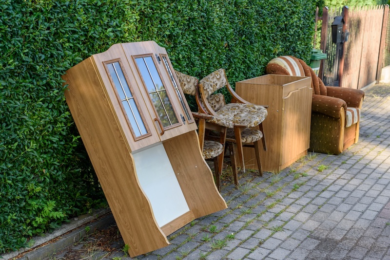 How to get rid of old furniture for free. Image shows pieces of old furniture resting up against a green hedge outside.