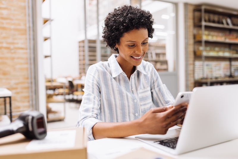 Offsite storage. Image shows a woman smiling at her phone with her laptop in front of her, working on here ecommerce business.