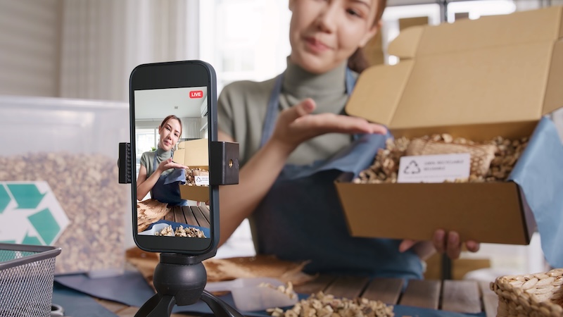 Storage for online sellers. Image shows a woman holding up a box with an item in and talking about it to her camera phone set up in front of her.