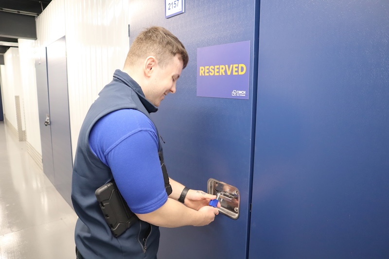 Watford short term storage. Image shows a cinch self storage employee putting a padlock on a storage unit that has a blue and orange reserved sign on it.
