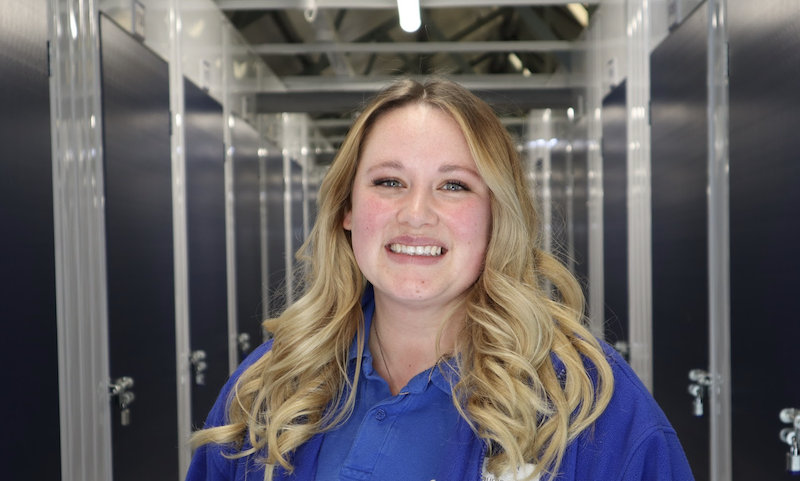 Best self storage in Letchworth. Image shows a female Cinch Self Storage employee standing in the middle of the corridor of storage units smiling to the camera.