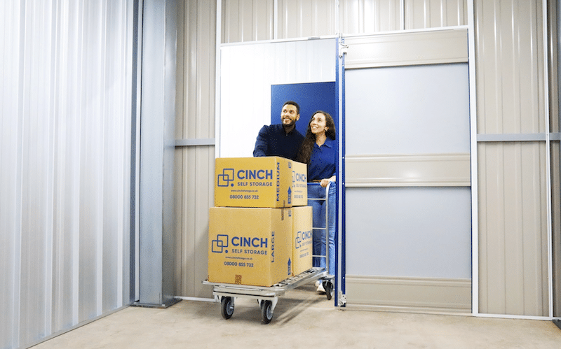 Storage units Sittingbourne. Image shows a couple walking into a storage unit with Cinch Storage boxes on their trolley.
