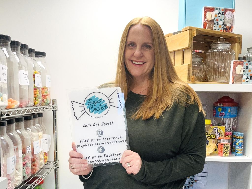 Sugar coated treats Cinch storage case study. Image shows the founder Vicky in her storage unit surrounded by sweets and holding up a sign that says 'Let's get social'. 