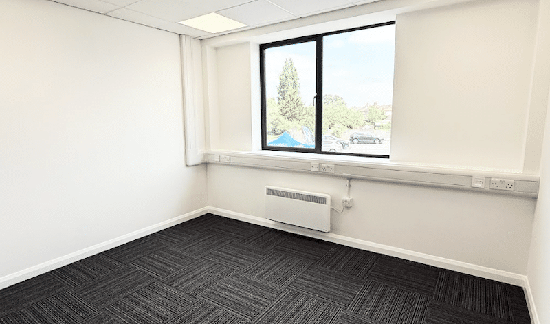 Office Swindon. Image shows an empty office with a large window, white walls and carpeted floor.