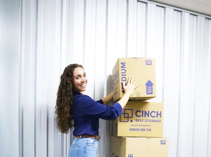 Storage rooms Dunstable. Image shows a woman stacking cardboard boxes inside her storage unit.