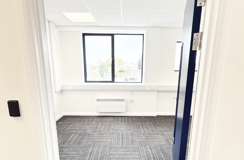 Office space to rent Leighton Buzzard. Image shows an empty office space with a large window and carpeted floor.