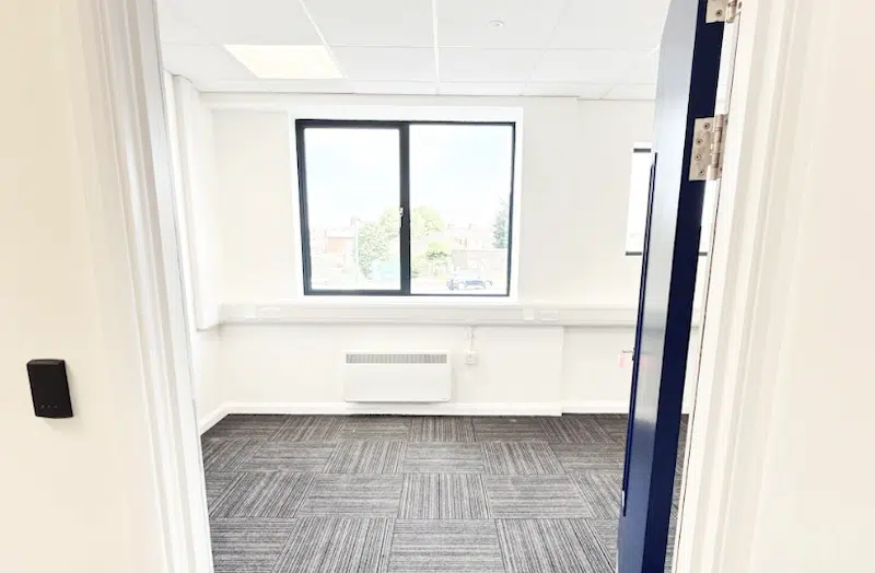 Office space to rent Leighton Buzzard. Image shows an empty office space with a large window and carpeted floor.