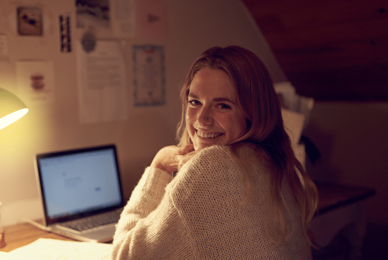 Storage facilities in Newcastle. Image shows a female student smiling to camera working on her laptop in her student bedroom.