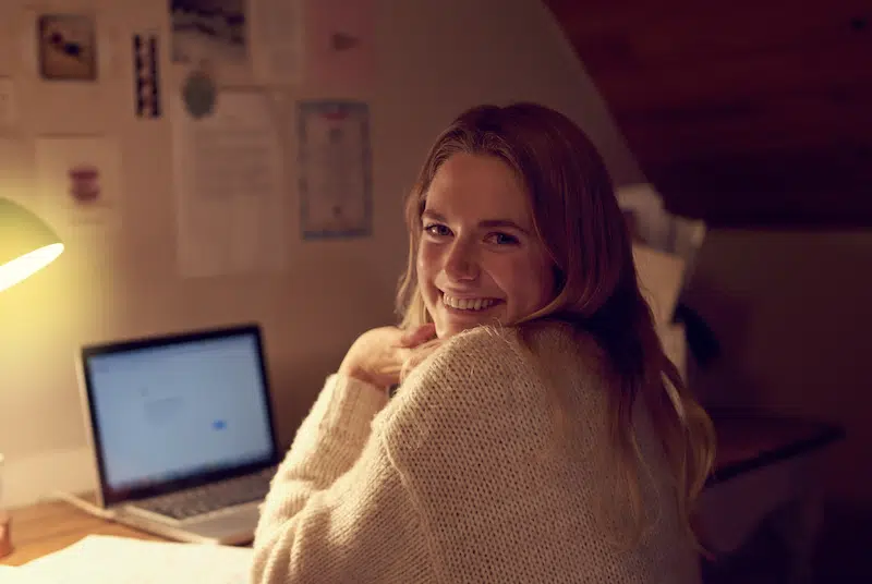 Storage facilities in Newcastle. Image shows a female student smiling to camera working on her laptop in her student bedroom.
