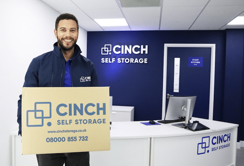Storage unit to rent Newcastle. Image shows a Cinch Self Storage employee in reception holding a Cinch Self Storage branded box.