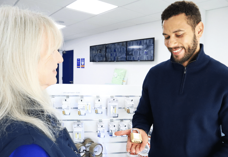 Choosing a secure storage facility in Brighton. Image shows a customer holding a padlock in the palm of his hand standing next to a Cinch Self Storage employee in the Box Shop filled with moving supplies.