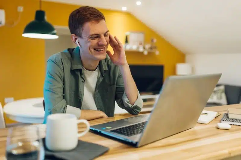 Storage rooms Shoreham. Image shows a young male freelancer having a video call with his colleagues using a laptop in the kitchen while working from home.
