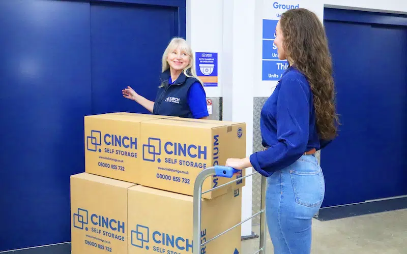 Short term storage Exeter. Image shows a Cinch Storage employee showing a woman with a full trolley of Cinch Self Storage cardboard boxes into the lift.