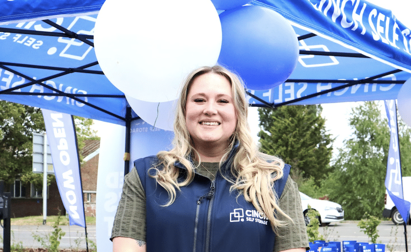 Student storage Swindon. Image shows a Cinch Self Storage employee standing smiling in front of balloons welcoming people to Cinch Storage Swindon.