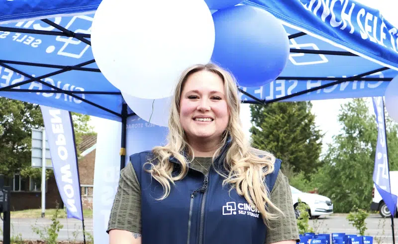 Student storage Swindon. Image shows a Cinch Self Storage employee standing smiling in front of balloons welcoming people to Cinch Storage Swindon.