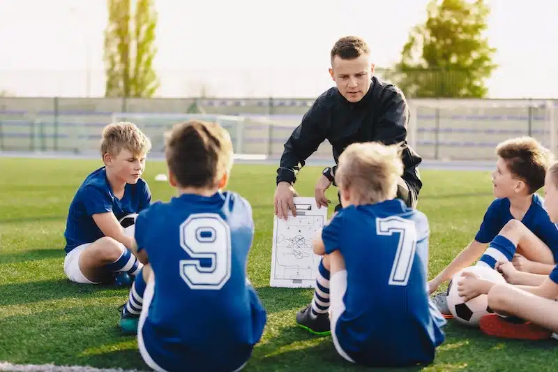 Gateshead storage. Image shows a football couch crouching on the ground talking to the kids he is teaching. 