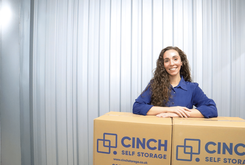 Low cost storage Shoreham. Image shows a woman leaning on Cinch Storage cardboard boxes in her storage unit.