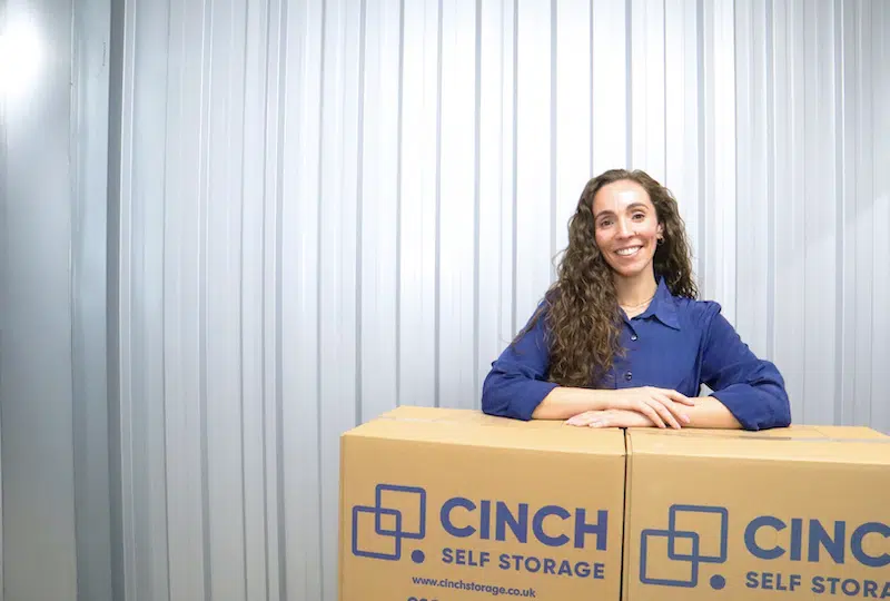 Low cost storage Shoreham. Image shows a woman leaning on Cinch Storage cardboard boxes in her storage unit. 
